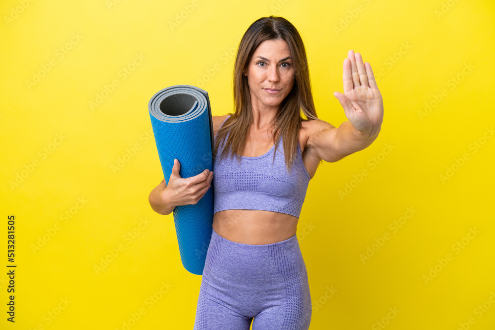 Sport woman going to yoga classes while holding a mat isolated non yellow background making stop gesture Sport woman going to yoga classes while holding a mat isolated non yellow background making stop gesture