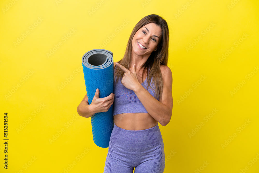 Sport woman going to yoga classes while holding a mat isolated non yellow background pointing to the side to present a product Sport woman going to yoga classes while holding a mat isolated non yellow background pointing to the side to present a product
