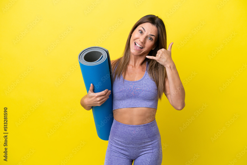 Sport woman going to yoga classes while holding a mat isolated non yellow background making phone gesture. Call me back sign Sport woman going to yoga classes while holding a mat isolated non yellow background making phone gesture. Call me back sign