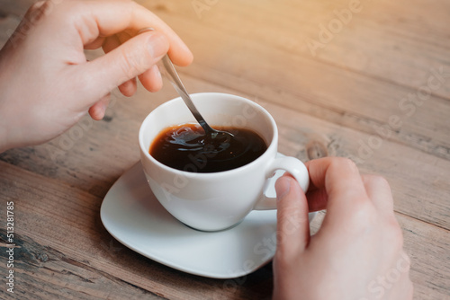 Close up of man enjoying in cup of morning coffee and mixing it with a spoon.