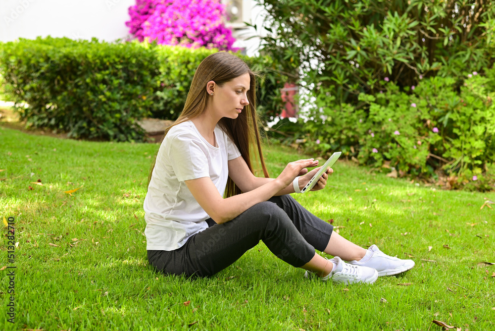 Beautiful girl sitting on the lawn holding a tablet. Work in nature. Beautiful girl sitting on the lawn holding a tablet. Work in nature.
