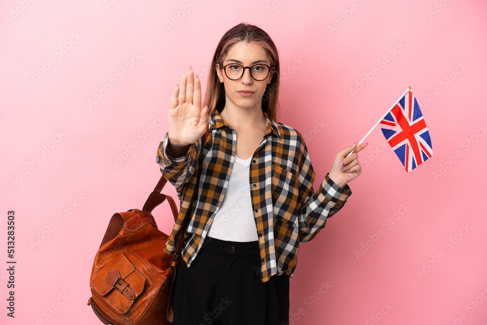 Young hispanic woman holding an United Kingdom flag isolated on pink background making stop gesture