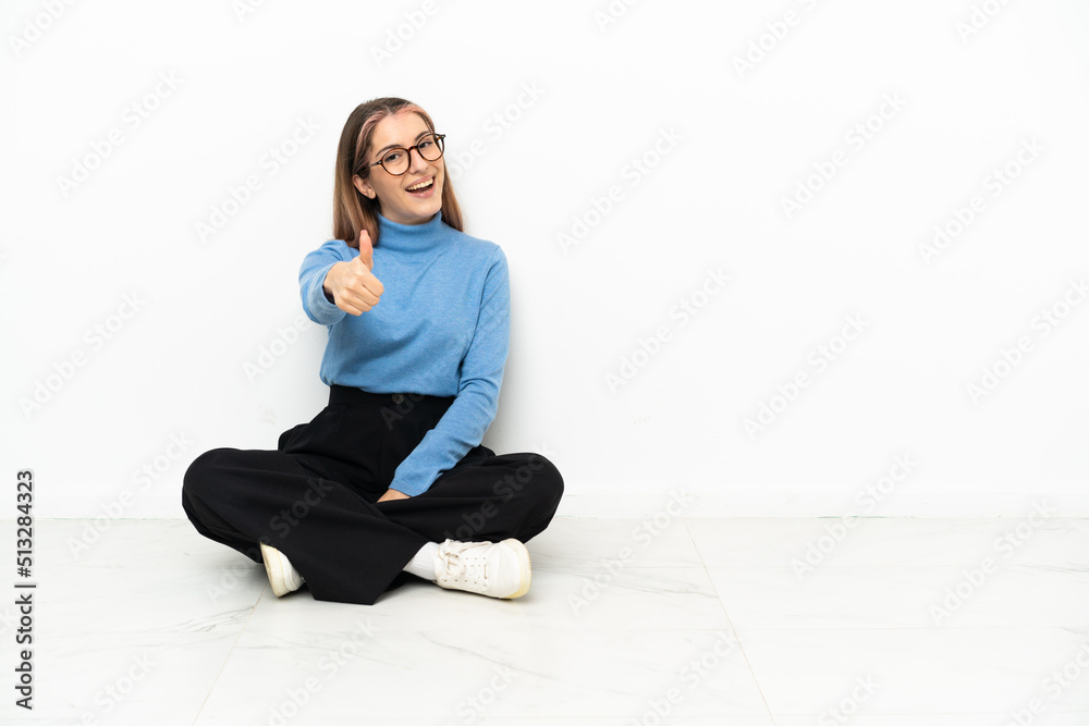 Young Caucasian woman sitting on the floor with thumbs up because something good has happened Young Caucasian woman sitting on the floor with thumbs up because something good has happened