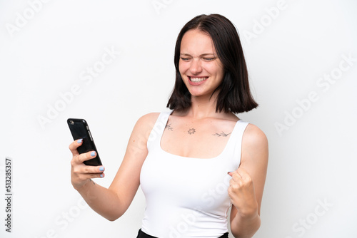 Young caucasian woman isolated on white background using mobile phone and doing victory gesture
