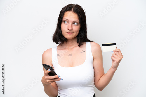 Young caucasian woman isolated on white background buying with the mobile with a credit card while thinking