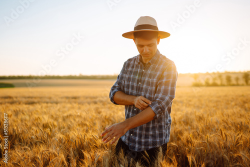Young Farmer in the hat in a wheat field. Agriculture, gardening or ecology concept. © maxbelchenko