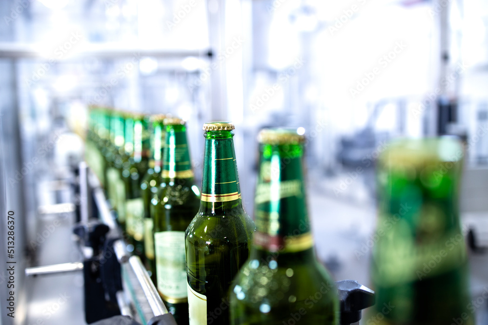 Beer bottles being transported on conveyer automated machine in beverage factory.