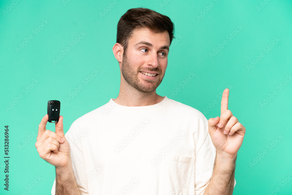 Young caucasian man holding car keys isolated on green background intending to realizes the solution while lifting a finger up Young caucasian man holding car keys isolated on green background intending to realizes the solution while lifting a finger up