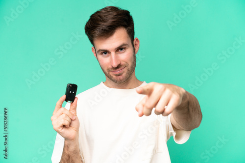 Young caucasian man holding car keys isolated on green background points finger at you with a confident expression