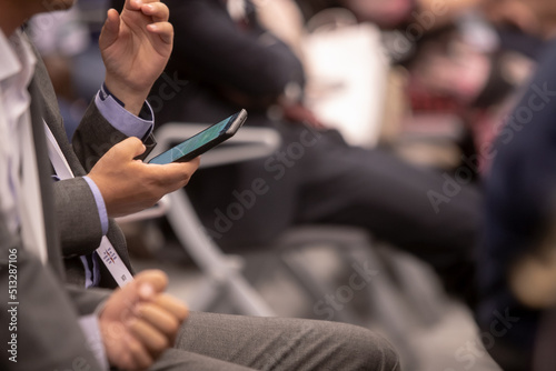 Audience in the conference hall. The man in the foreground looking into your phone