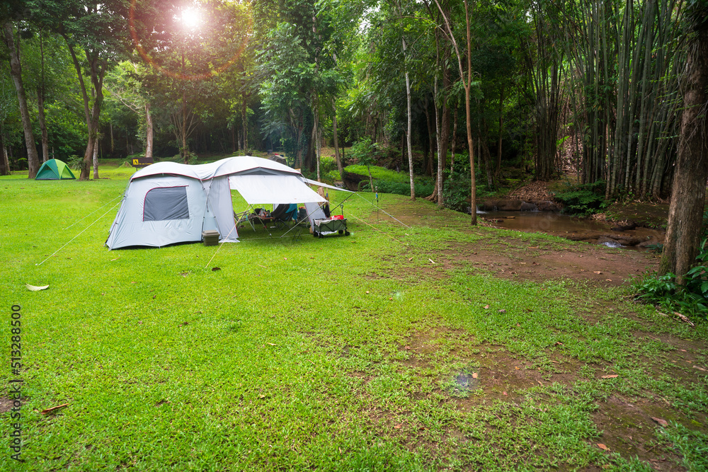 camping cabin tent on stream campground and tree in nature green forest and summer camp to holiday relax or vacation travel trip with family trekking on lawn and morning sunlight at Pha Tad Waterfall