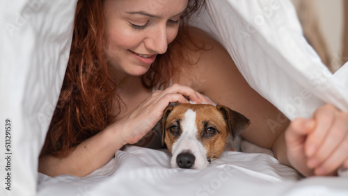 Caucasian red-haired woman sleeps in an embrace with a jack russell terrier dog on a white sheet.
