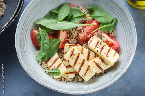 Grey bowl with quinoa, grilled halloumi cheese, fresh spinach and red tomatoes, close-up, selective focus photo