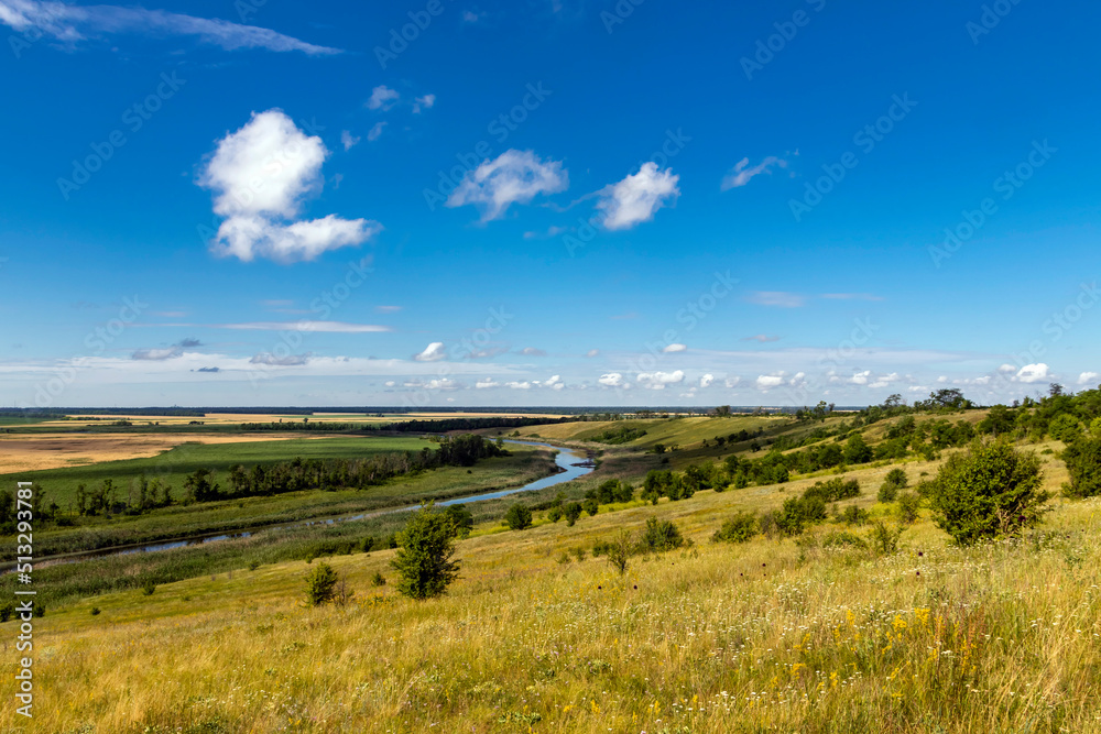 Sunny summer landscape with a river. Green hills and meadows. Fields of ripe wheat.