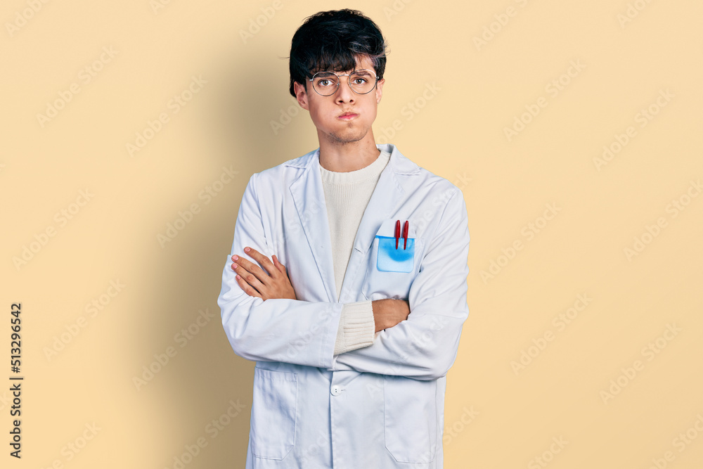 Handsome hipster young man with crossed arms wearing doctor uniform puffing cheeks with funny face. mouth inflated with air, catching air. Handsome hipster young man with crossed arms wearing doctor uniform puffing cheeks with funny face. mouth inflated with air, catching air.