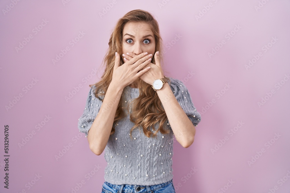 Beautiful blonde woman standing over pink background shocked covering mouth with hands for mistake. secret concept. Beautiful blonde woman standing over pink background shocked covering mouth with hands for mistake. secret concept.
