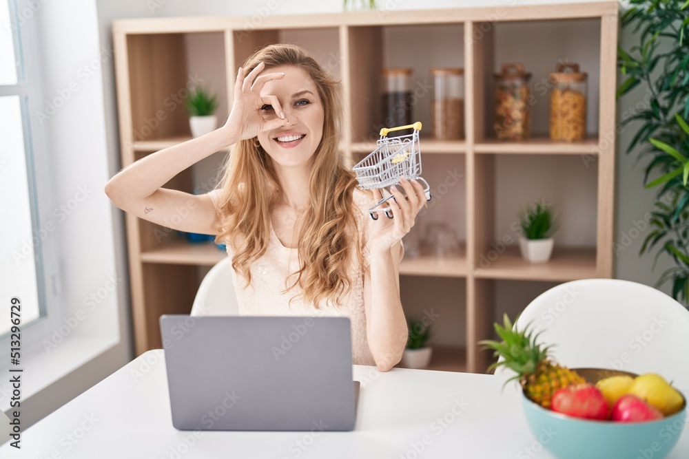 Beautiful blonde woman shopping online with laptop smiling happy doing ok sign with hand on eye looking through fingers
