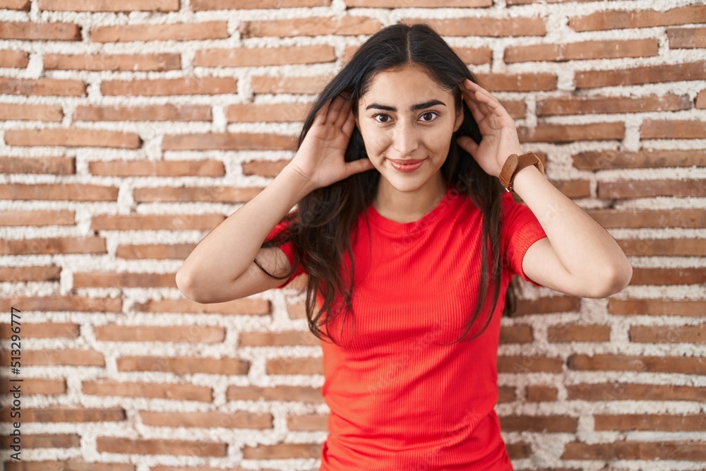 Young teenager girl standing over bricks wall trying to hear both hands on ear gesture, curious for gossip. hearing problem, deaf Young teenager girl standing over bricks wall trying to hear both hands on ear gesture, curious for gossip. hearing problem, deaf