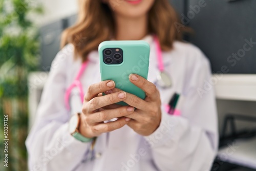 Young woman wearing doctor uniform using smartphone at clinic