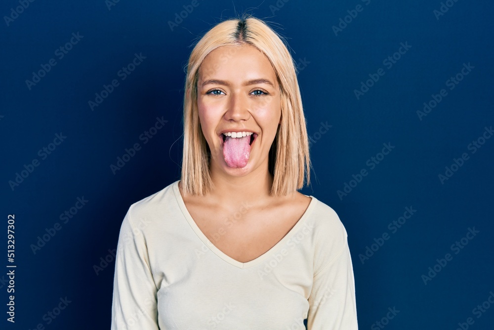 Beautiful blonde woman wearing casual sweater sticking tongue out happy with funny expression. emotion concept. Beautiful blonde woman wearing casual sweater sticking tongue out happy with funny expression. emotion concept.