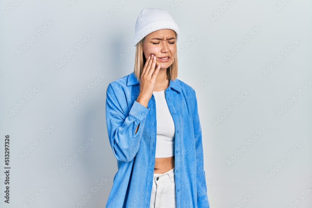 Beautiful blonde woman wearing wool hat touching mouth with hand with painful expression because of toothache or dental illness on teeth. dentist Beautiful blonde woman wearing wool hat touching mouth with hand with painful expression because of toothache or dental illness on teeth. dentist