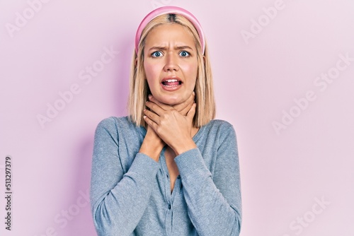 Beautiful blonde woman standing over pink background shouting and suffocate because painful strangle. health problem. asphyxiate and suicide concept.