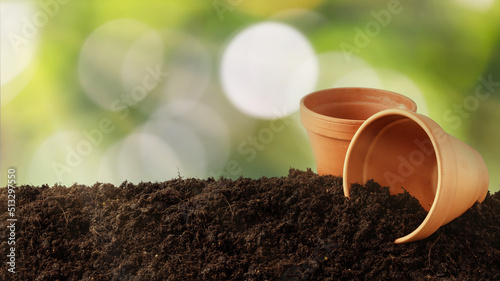 Black soil with clay pots in sunlight rays on blurred foliage background. Gardening and planting season concept.