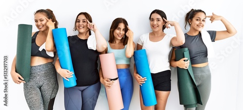 Group of women holding yoga mat standing over isolated background smiling pointing to head with one finger, great idea or thought, good memory © Krakenimages.com
