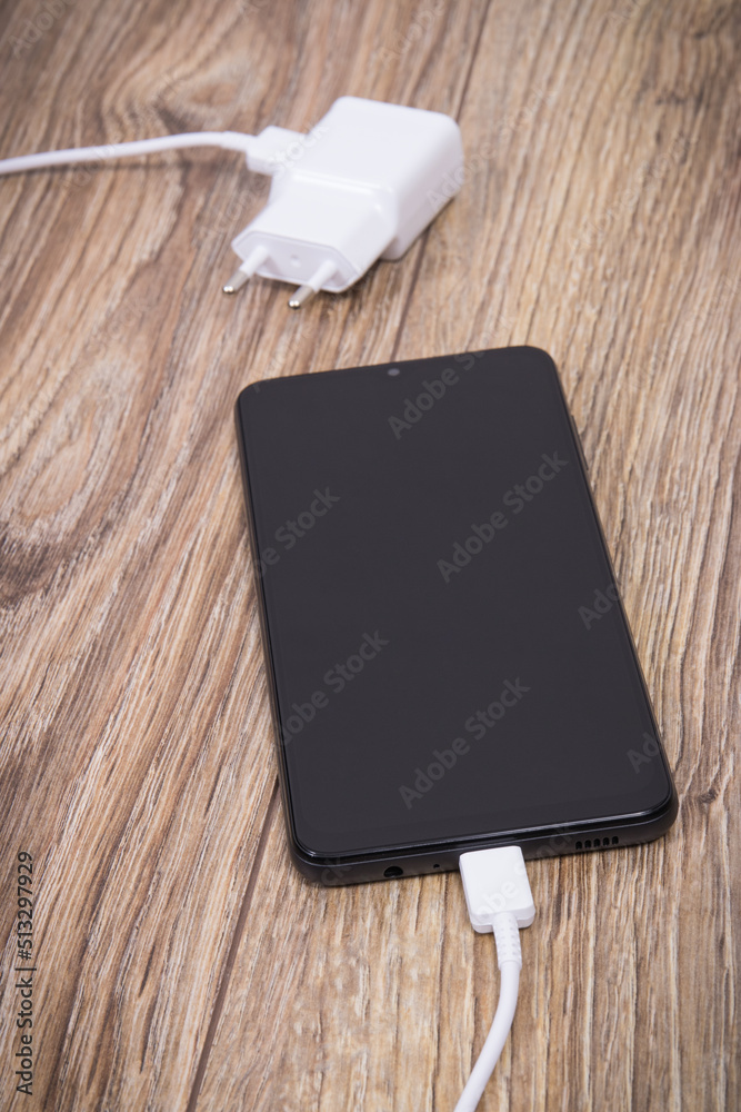 Black smartphone and charger using to charge empty battery. Various devices charging concept Black smartphone and charger using to charge empty battery. Various devices charging concept