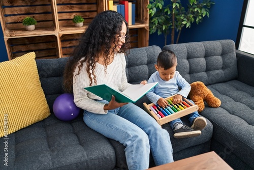 Mother and son reading book sitting on sofa at home