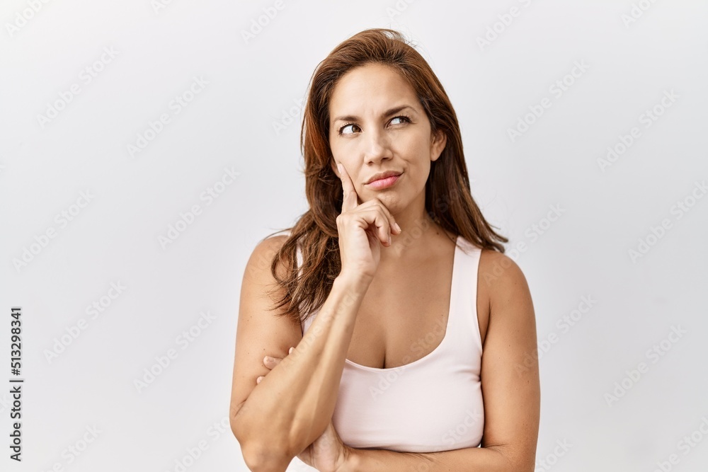 Middle age hispanic woman standing over isolated background with hand on chin thinking about question, pensive expression. smiling with thoughtful face. doubt concept. Middle age hispanic woman standing over isolated background with hand on chin thinking about question, pensive expression. smiling with thoughtful face. doubt concept.