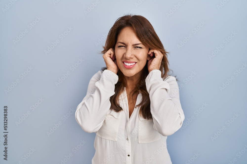 Hispanic woman standing over isolated background covering ears with fingers with annoyed expression for the noise of loud music. deaf concept. Hispanic woman standing over isolated background covering ears with fingers with annoyed expression for the noise of loud music. deaf concept.