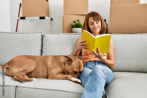 Young caucasian woman reading book sitting on sofa with dog at home
