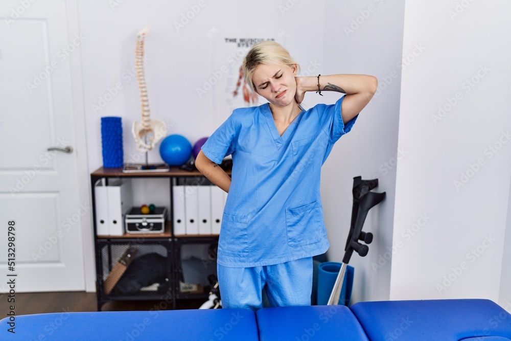 Young physiotherapist woman working at pain recovery clinic suffering of neck ache injury, touching neck with hand, muscular pain Young physiotherapist woman working at pain recovery clinic suffering of neck ache injury, touching neck with hand, muscular pain