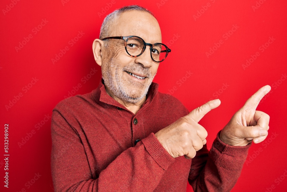 Handsome mature man wearing casual sweater and glasses smiling and looking at the camera pointing with two hands and fingers to the side. Handsome mature man wearing casual sweater and glasses smiling and looking at the camera pointing with two hands and fingers to the side.
