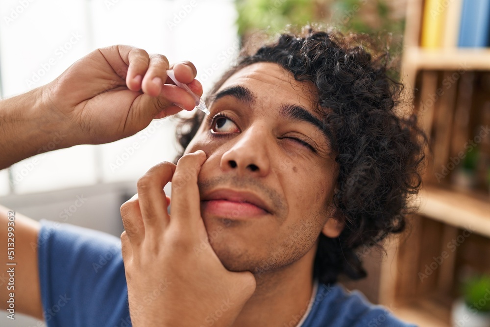 Young hispanic man applying eyes drop sitting on sofa at home Young hispanic man applying eyes drop sitting on sofa at home