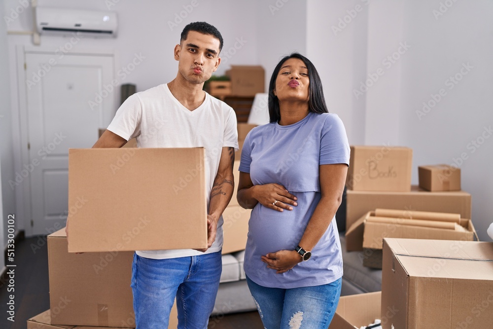 Young hispanic couple expecting a baby moving to a new home looking at the camera blowing a kiss being lovely and sexy. love expression.