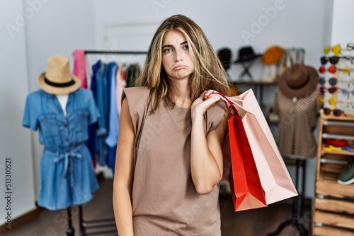Young blonde woman holding shopping bags at retail shop depressed and worry for distress, crying angry and afraid. sad expression.