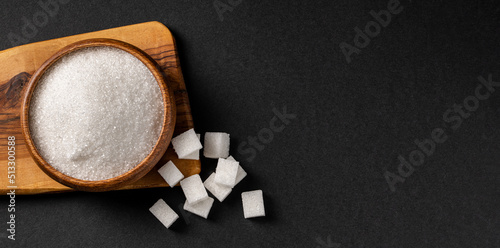 Granulated sugar and sugar cubes in wooden bowl on dark background