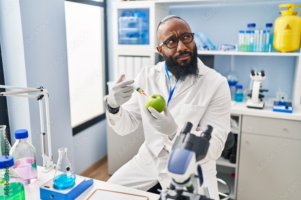 African american man working at scientist laboratory with apple smiling looking to the side and staring away thinking. African american man working at scientist laboratory with apple smiling looking to the side and staring away thinking.