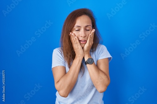 Brunette woman standing over blue background tired hands covering face, depression and sadness, upset and irritated for problem