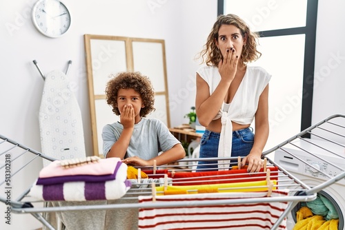 Young woman and son doing laundry at clothesline covering mouth with hand, shocked and afraid for mistake. surprised expression