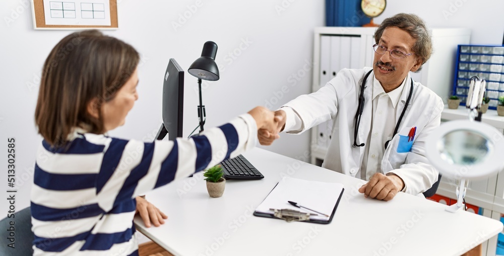 Obraz premium Middle age man and woman wearing doctor uniform having medical consultation shake hands at clinic