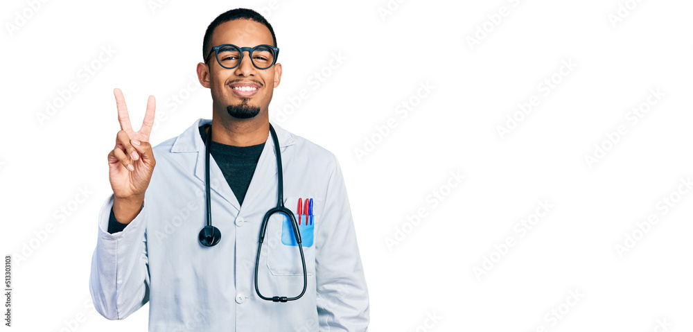 Young african american man wearing doctor uniform and stethoscope smiling looking to the camera showing fingers doing victory sign. number two.