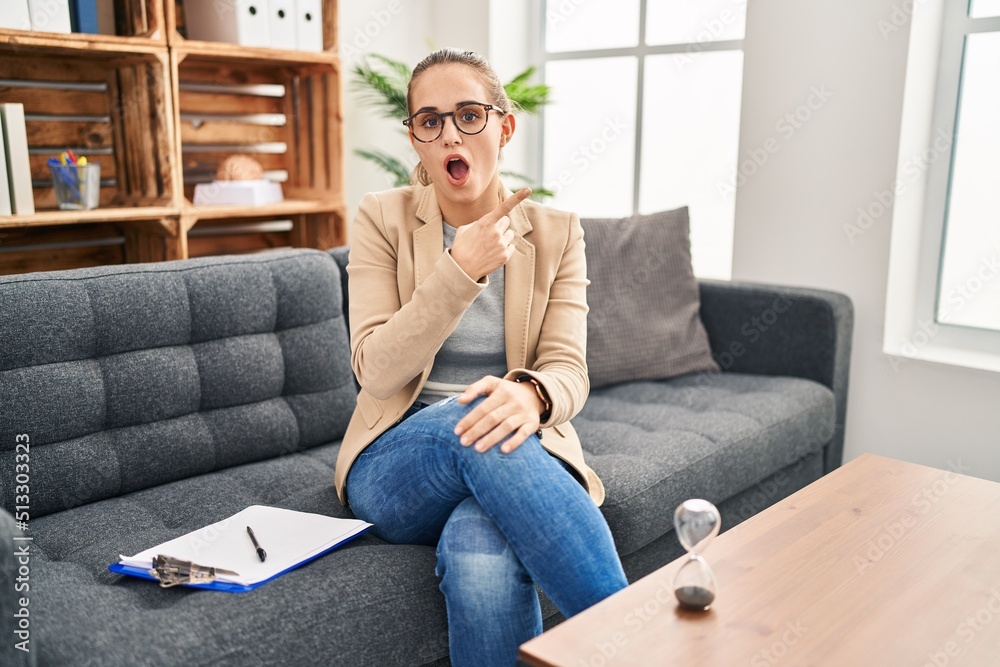Young woman working at consultation office surprised pointing with finger to the side, open mouth amazed expression. Young woman working at consultation office surprised pointing with finger to the side, open mouth amazed expression.