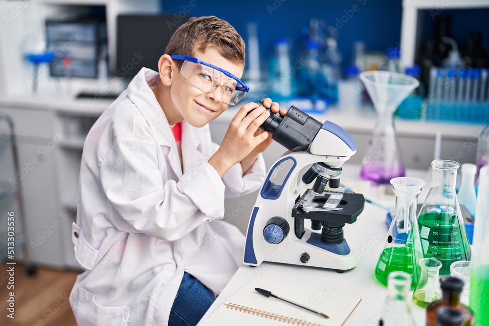 Blond child wearing scientist uniform using microscope at laboratory Blond child wearing scientist uniform using microscope at laboratory
