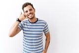 Handsome young man standing over isolated background smiling doing phone gesture with hand and fingers like talking on the telephone. communicating concepts.