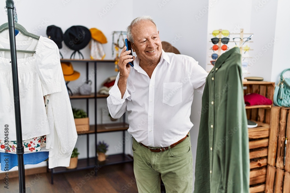 Senior man customer talking on the smartphone holding shirt at clothing store