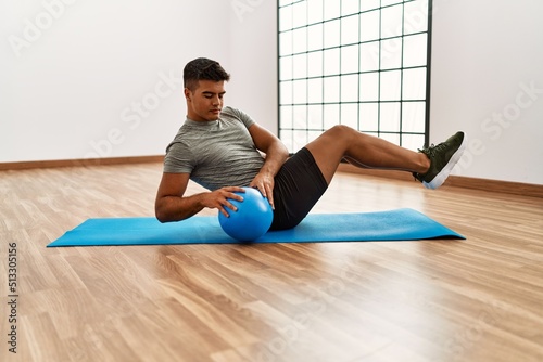 Young hispanic man training abs exercise using ball at sport center