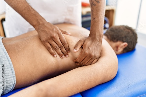 Two men physiptherapist and patient having rehab session massaging back at clinic